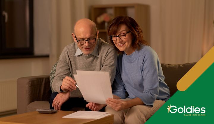 Um homem e uma mulher idosos estão sentados em um sofá, sorrindo e olhando um documento juntos, ilustrando o post "Educação financeira na terceira idade: Viva com mais tranquilidade"