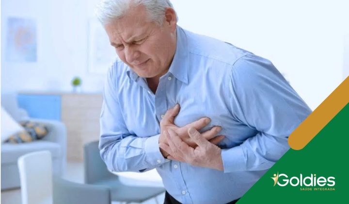 Um homem idoso de camisa azul aperta o peito com dor em um ambiente doméstico, ilustrando o post "Infarto Do Miocárdio: o que é, sintomas e fatores de risco"