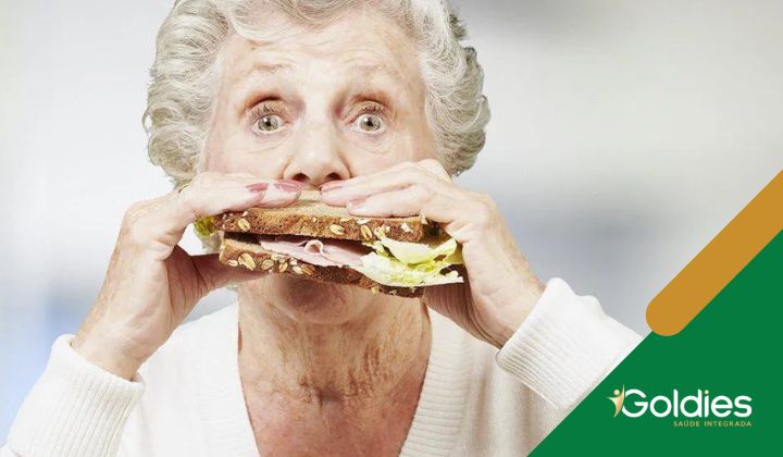 Idoso comendo um sanduíche grande com alface, queijo e carne, ilustrando o post "Obesidade na terceira idade: principais causas e como tratar"