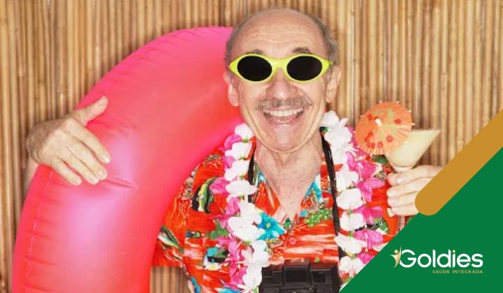 Homem idoso usando óculos escuros e uma camisa florida, segurando uma bebida com um guarda-chuva e um anel inflável, ilustrando o post "Viajar na Terceira idade – A beleza de conhecer novos lugares"