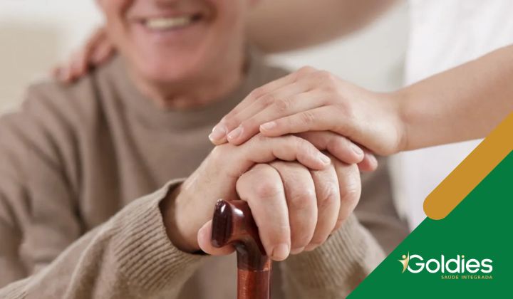 Uma pessoa idosa segura uma bengala de madeira, com as mãos gentilmente apoiadas sobre as suas. Uma pessoa fica perto, colocando uma mão de apoio em seu ombro, ilustrando o post "Direito do idoso: benefícios das leis de incentivo"