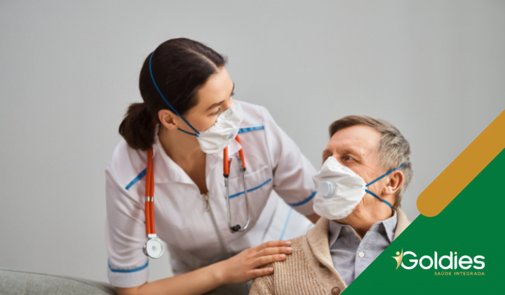 Profissional de saúde de jaleco branco com estetoscópio confortando um idoso usando máscara, ilustrando o post "Doenças Crônicas e COVID-19"