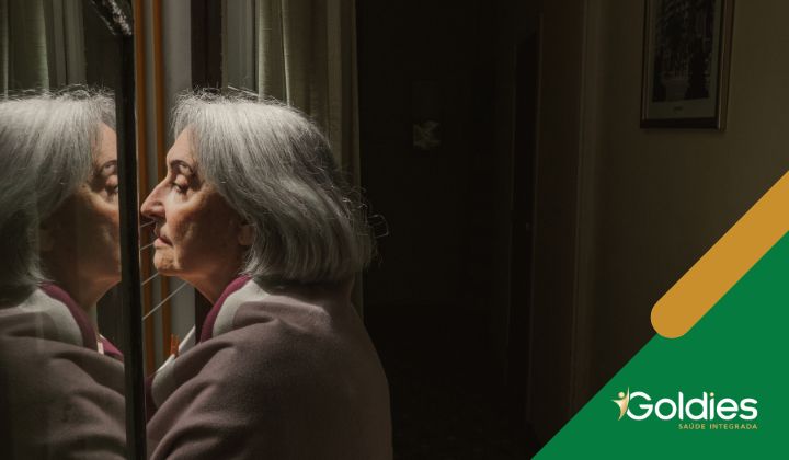 Mulher idosa com cabelos brancos e blusa rosa olha para seu reflexo em uma janela, ilustrando o post "A demência pode ser prevenida em qualquer idade"