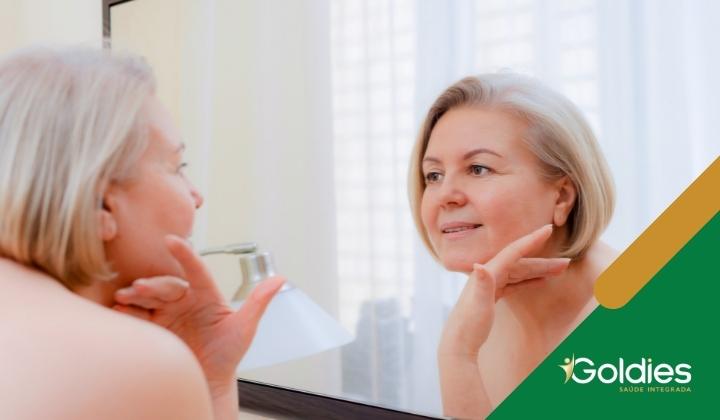 Uma mulher madura, com cabelo curto, sorri enquanto olha seu reflexo em um espelho, ilustrando o post "Vaidade após os 60 anos"