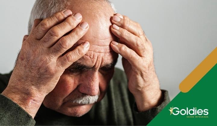 Homem idoso com cabelos grisalhos segurando a cabeça entre as mãos, parecendo angustiado ou pensativo, ilustrando o post "7 hábitos que reduzem o risco de demência"