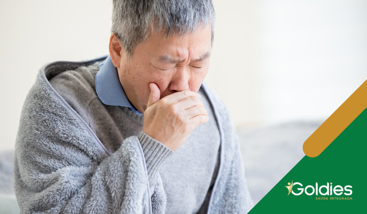 Idoso tossindo com a mão sobre o rosto, ilustrando o post "Pneumonia em seniores: tudo o que você precisa saber"