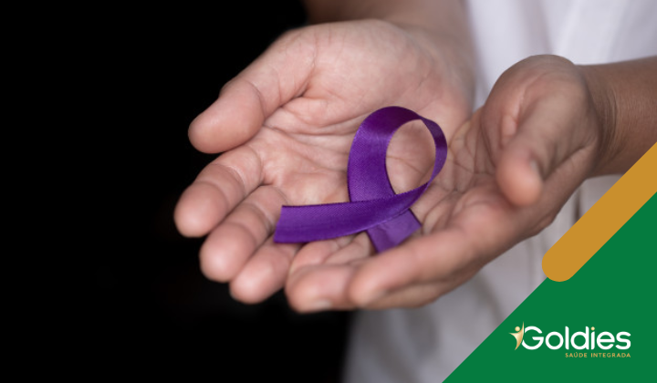 Mãos segurando uma fita roxa de conscientização, simbolizando apoio a causas como conscientização sobre violência doméstica e epilepsia. A imagem apresenta o logotipo da Goldies Saúde Integrada no canto inferior direito.