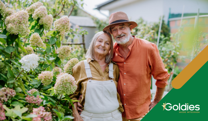 Um casal de idosos está sorrindo em um jardim cheio de hortênsias floridas. ilustrando o artigo "Atividades para Idosos: 10 dicas de lazer para a saúde do senior"