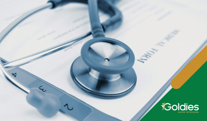 Um estetoscópio repousa sobre um formulário médico, simbolizando assistência médica e diagnósticos. No canto inferior direito, há um logotipo verde e amarelo com a palavra Goldies e a frase SAÚDE INTEGRADA.