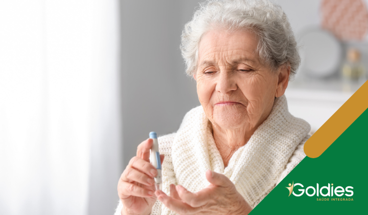 Uma mulher idosa com um suéter branco usa um medidor de glicose em casa, ilustrando o post "Controle do Diabetes na Terceira Idade: Peculiaridades e Cuidados Especiais"