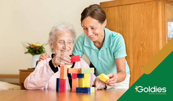 Uma senhora idosa e uma cuidadora estão sorrindo enquanto brincam com blocos de madeira coloridos em uma mesa ilustrando o artigo "Terapia ocupacional para idosos: Seus efeitos na qualidade de vida"